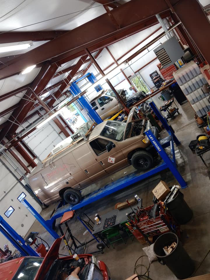 Inside the shop, vehicles up on blue two post lifts across several bays
