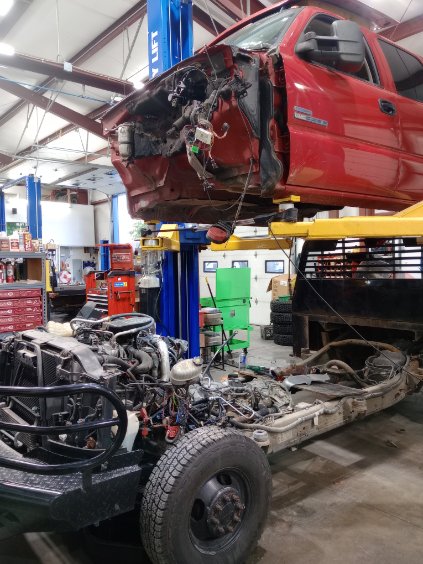 A red truck cab lifted clear of its frame on a lift, with the engine and chassis exposed below