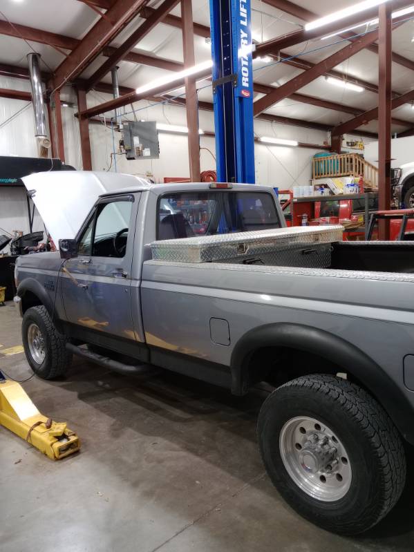 A gray Ford pickup with its hood open beside a blue Rotary lift